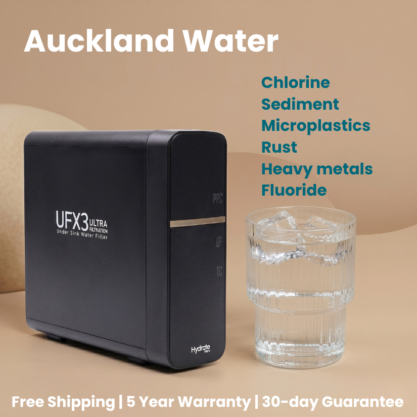 Black water filter with a glass of water on a beige background, featuring Auckland Water branding.
