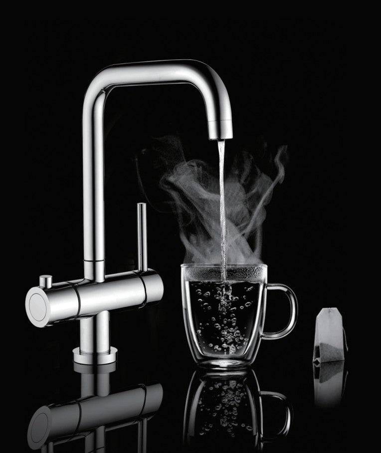 A modern chrome double-handle faucet with boiling water running into a clear glass mug, shown on a black reflective background with a tea bag beside the mug.