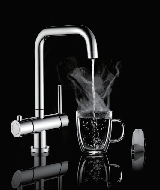 A modern chrome double-handle faucet with boiling water running into a clear glass mug, shown on a black reflective background with a tea bag beside the mug.